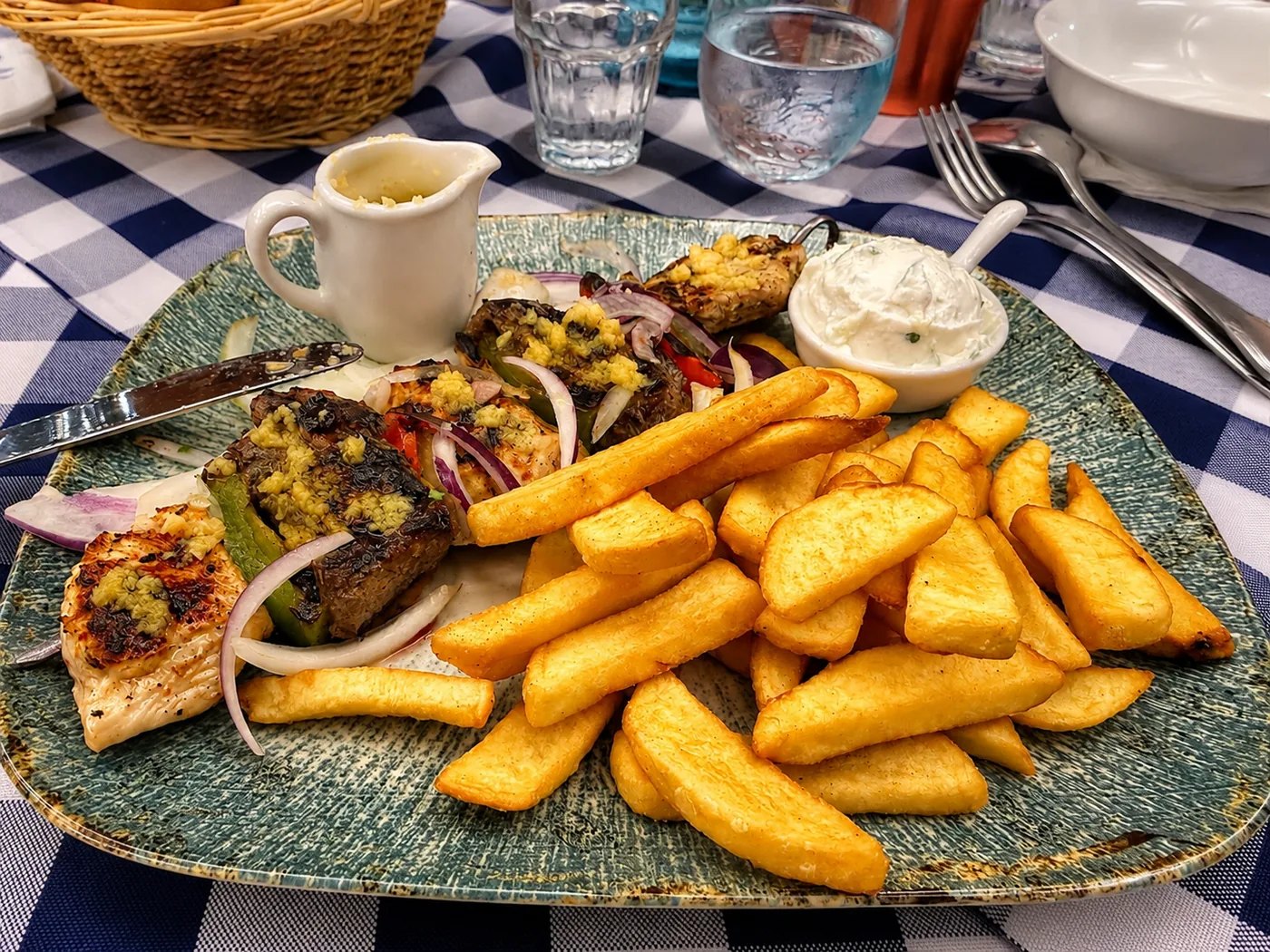 Mediterraner Grillteller: Gegrillte Spezialitäten mit Pommes, Dip und frischen Zwiebeln – großzügig serviert.