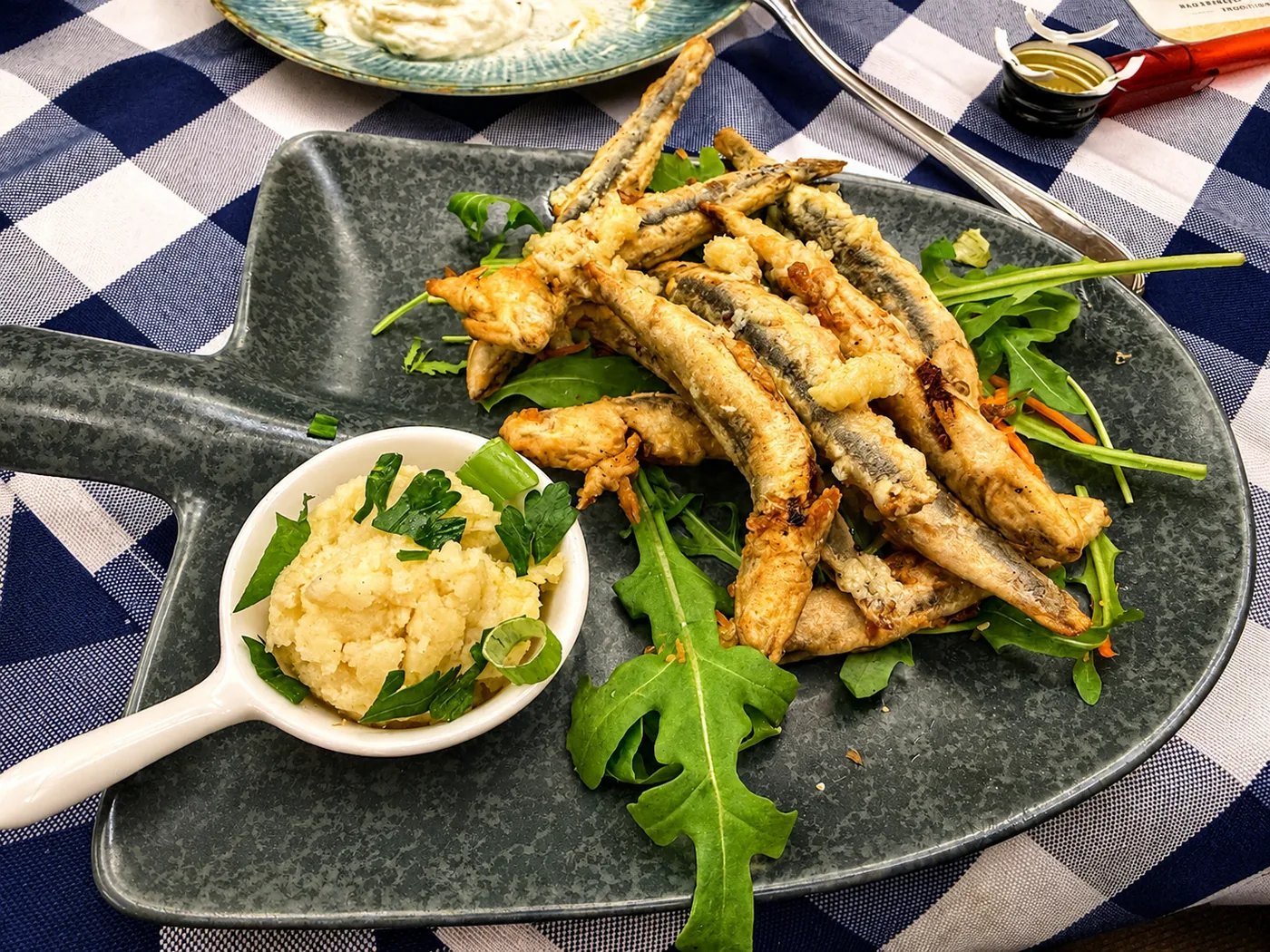 Frittierte Fischspezialitäten: Kleine, kross gebratene Fische mit Dip und frischem Rucola.